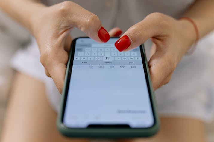 What Does 'Delivered' Status Mean on Your iPhone? 3 Close-up of hands with red nail polish typing on a smartphone’s on-screen keyboard.