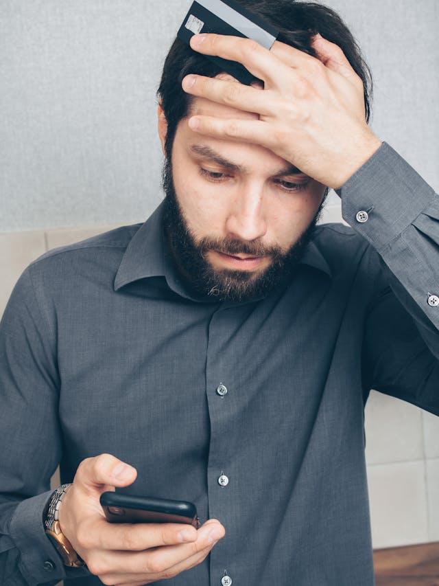 What Does 'Delivered' Status Mean on Your iPhone? 4 Worried man holding a credit card and looking at his phone, hand on forehead