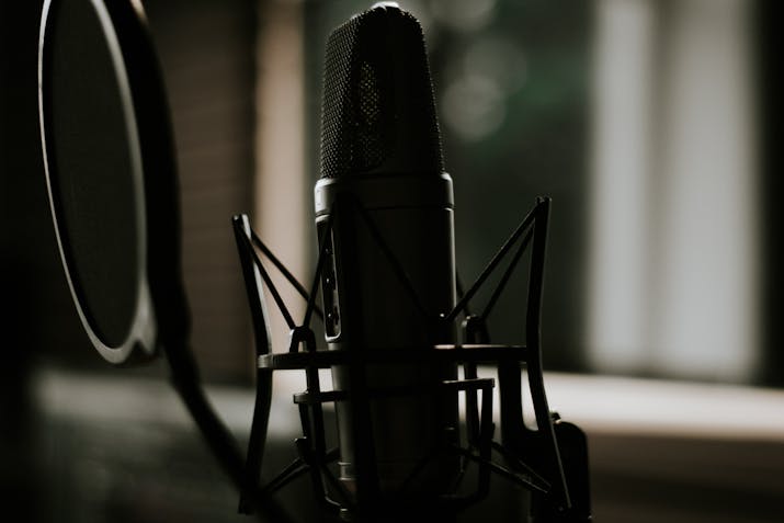 How to Avoid Choppy in GarageBand Playback 2 Close-up of a studio condenser microphone with shock mount and pop filter in dim lighting.