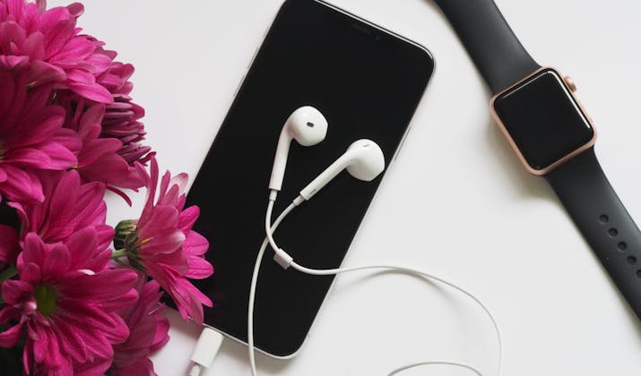 Apple Watch Black Screen - Troubleshooting Tips 3 Flat lay of iPhone, Apple EarPods, and a rose gold Apple Watch next to pink flowers.