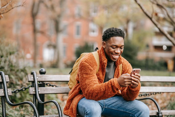 What Does 'Delivered' Status Mean on Your iPhone? 6 Smiling man sitting on a park bench, looking down at his phone while texting.