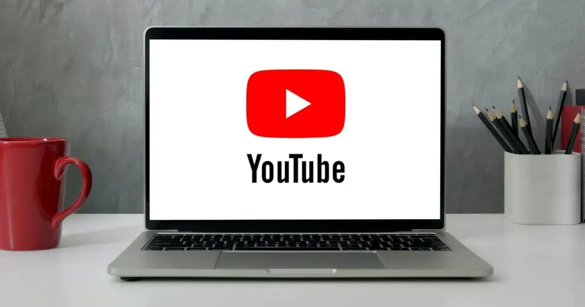 How to Download and Install Youtube App for Mac 1 Laptop displaying YouTube logo on screen with red mug and pencil holder on desk