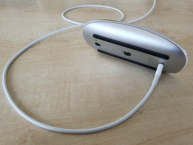 A mouse laid on its side connected to a cable attached to a computer on a table.