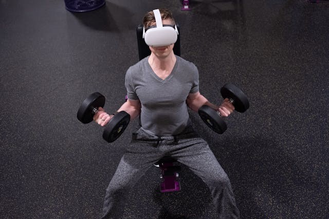 A man lifting weights in a gym with a white oculus headset on.